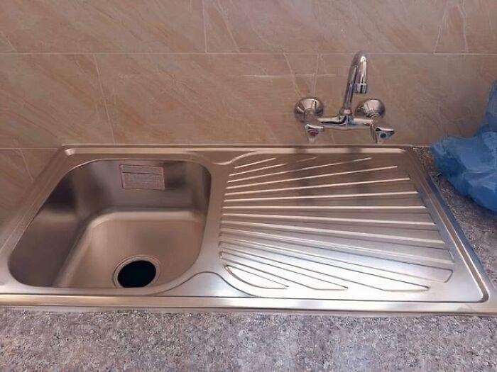A kitchen sink with the faucet installed off-center and far from the basin, a ridiculous You Had One Job fail.
