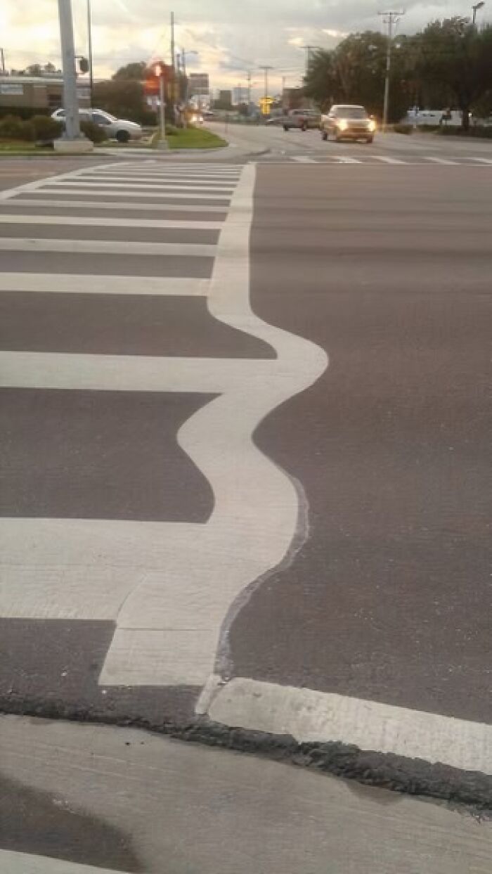 A wavy and incorrectly painted crosswalk line on a road, a ridiculous You Had One Job fail due to lack of common sense.