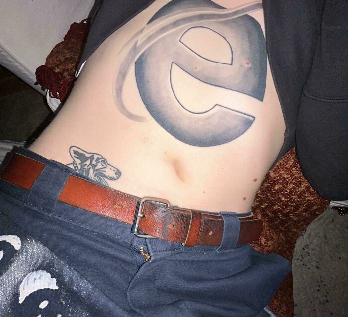 A large tattoo of the old Internet Explorer logo on a person's torso, with a small dog tattoo nearby. An example of a questionable tattoo idea.