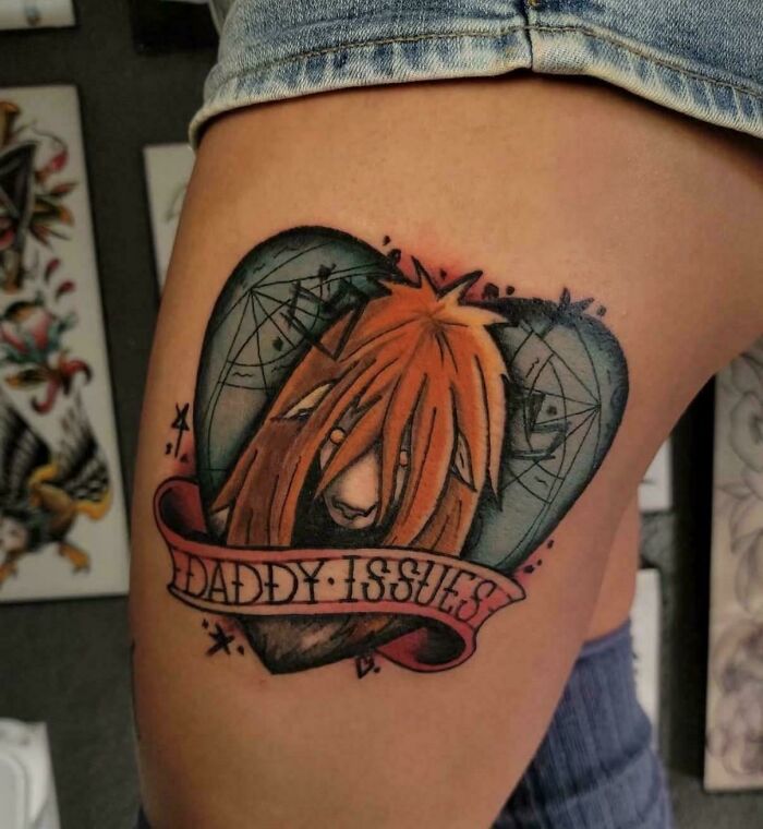 A detailed tattoo on a person's thigh depicting a character's head within a heart, with the text 'DADDY ISSUES'. A questionable tattoo idea.