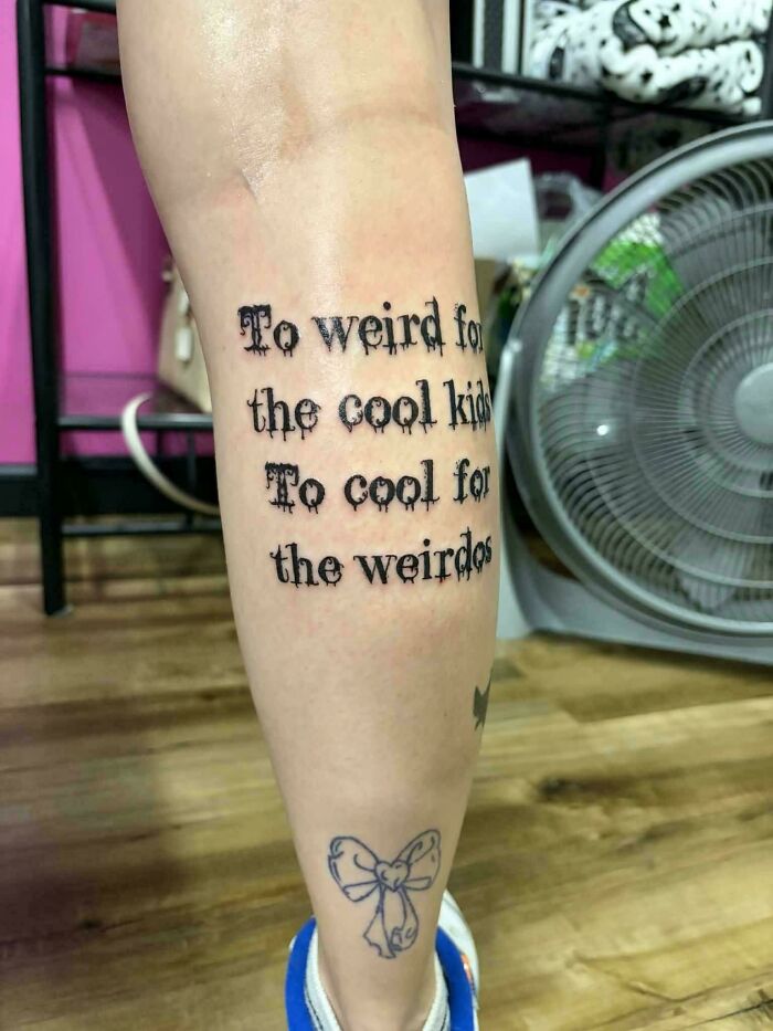 A leg with a text tattoo that reads To weird for the cool kids, To cool for the weirdos, demonstrating a tattoo artist's talent.