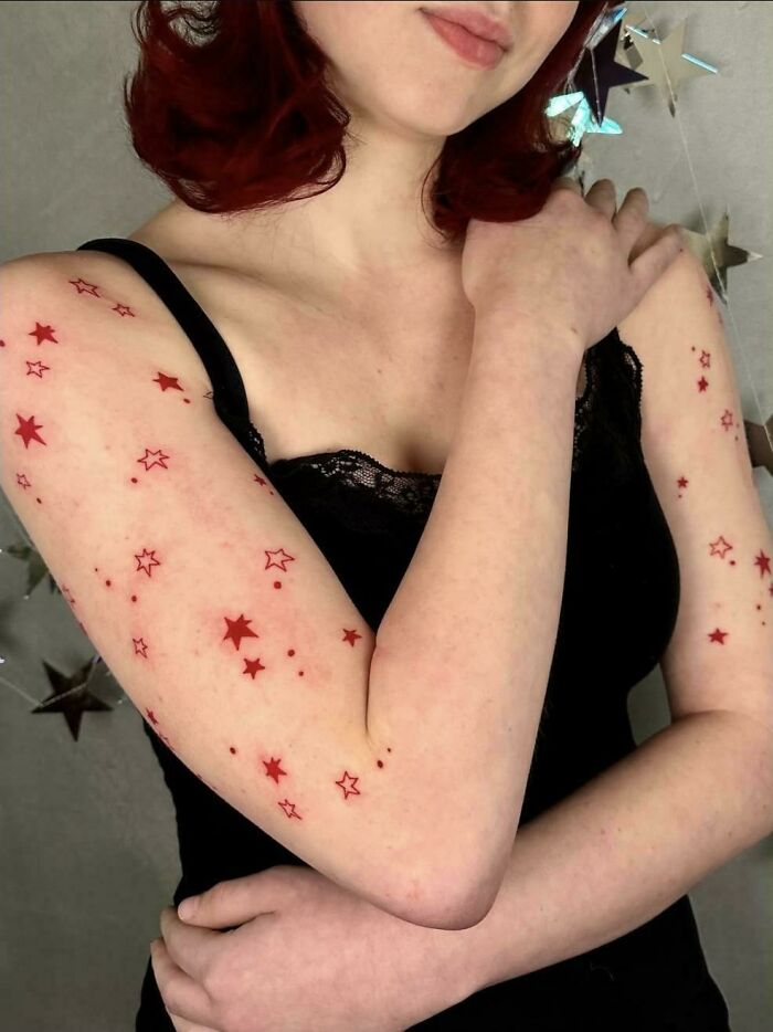 A woman with numerous small red star tattoos covering her arms, showcasing a tattoo artist's talent.