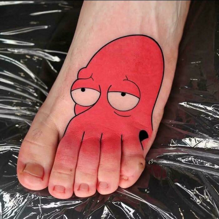 A cartoonish red octopus tattoo on a foot, with tentacles wrapping around toes, demonstrating the tattoo artist's talent.