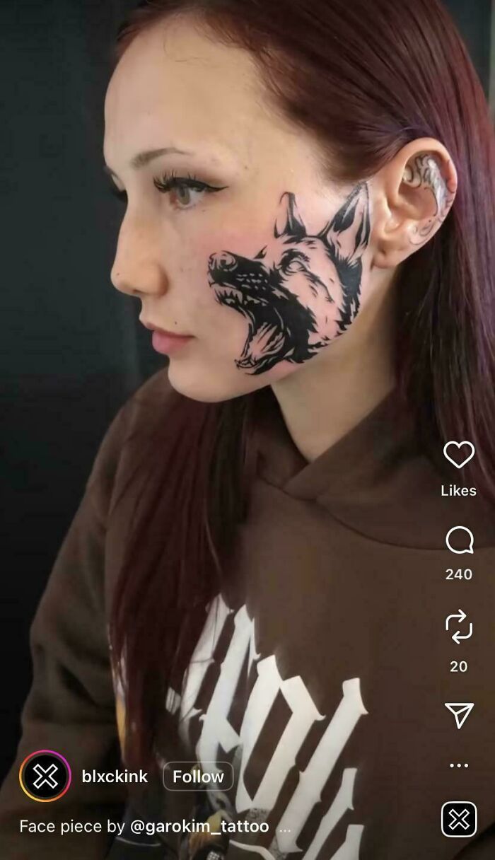 A bold black tattoo of a wolf's head with an open mouth on a woman's cheek, highlighting the tattoo artist's talent.