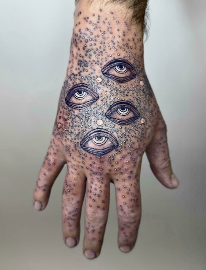 A tattoo artist's work on a hand tattoo with questionable ideas featuring four realistic eyes amidst a dotted texture, creating an unusual design.