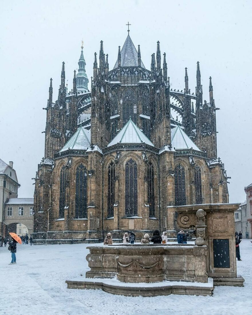 Snow-covered St. Vitus Cathedral with spires and tourists nearby