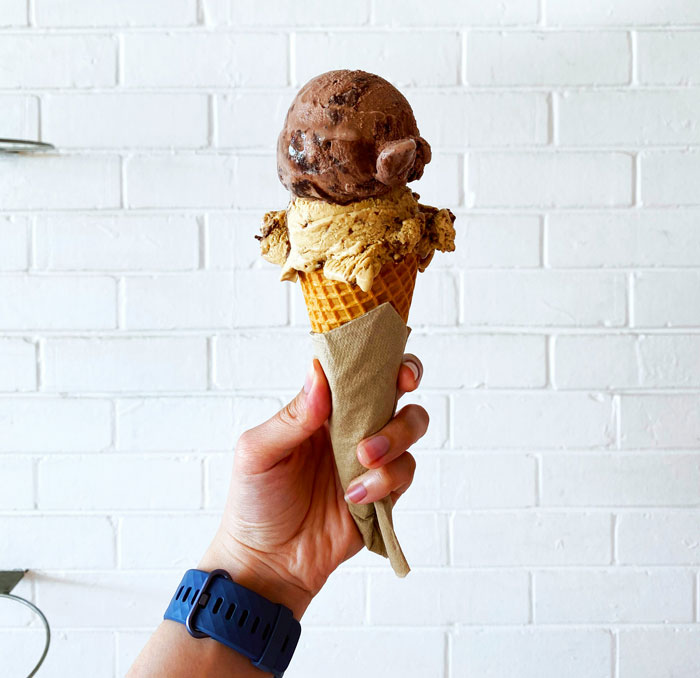 Hand holding double scoop ice cream cone with chocolate and coffee flavors