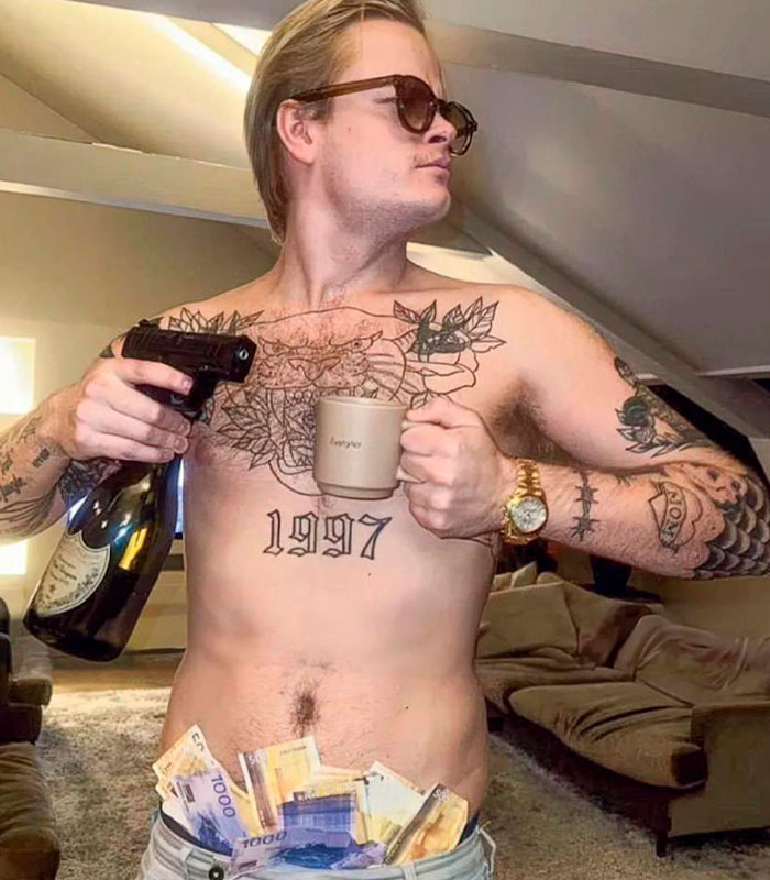 Tattooed young man with gun and money posing indoors