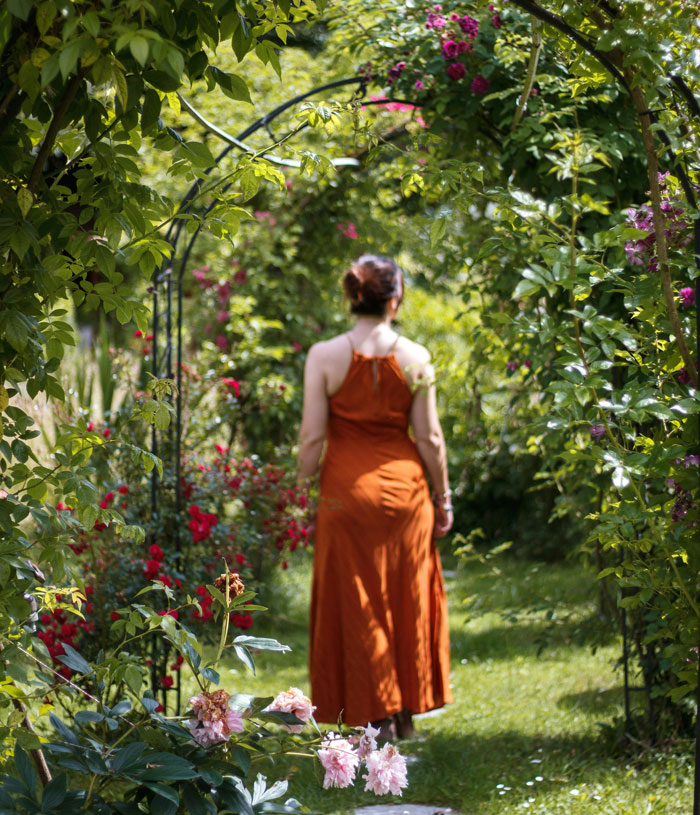 Woman in orange dress walking in a garden surrounded by greenery