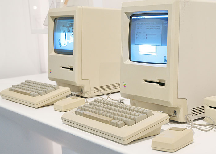 Two vintage Macintosh computers on a white desk, iconic machines for solving serious problems.