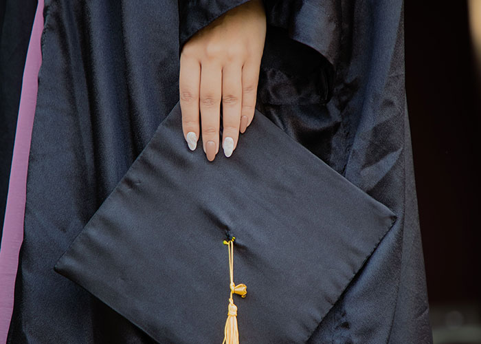 A person in a graduation gown holding a cap, signifying kids reaching independence after losing contact with parents.