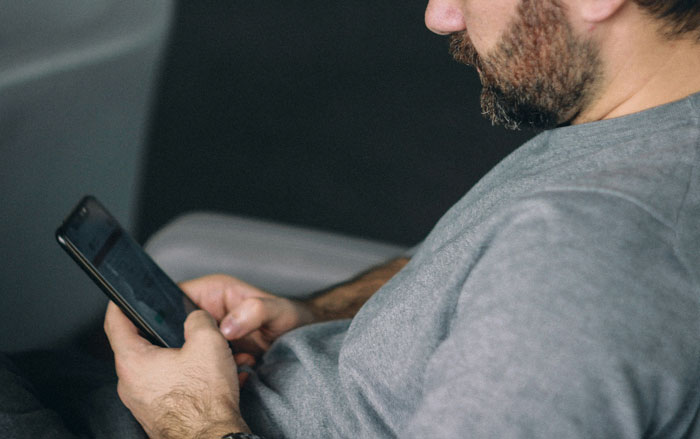 A man with a beard looking at his phone, potentially reading or sharing DNA testing stories.
