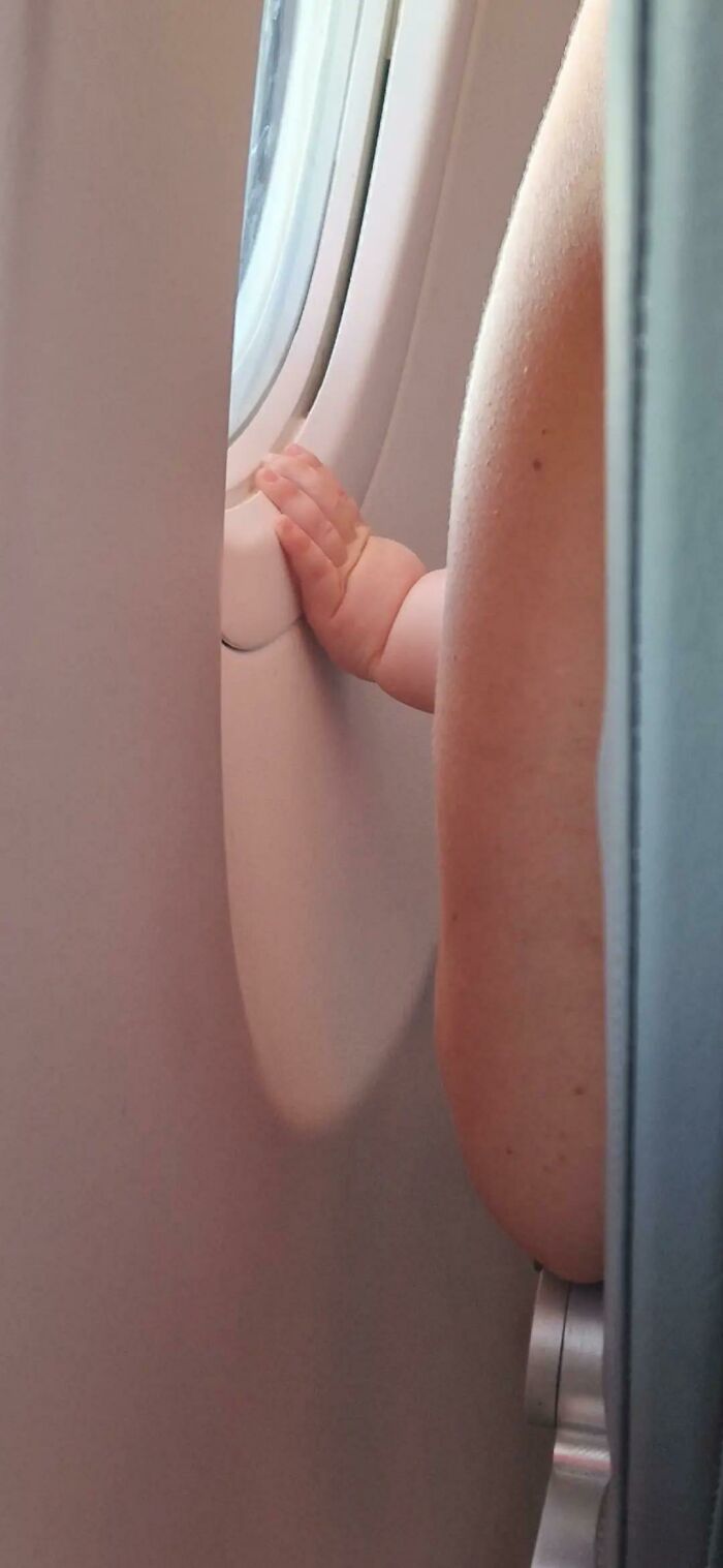 A baby's hand reaching towards an airplane window, a wholesome photo trend capturing tender moments with strangers.