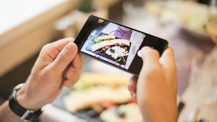 Person taking a photo of their meal with a smartphone on a date, highlighting acceptable actions during dating.