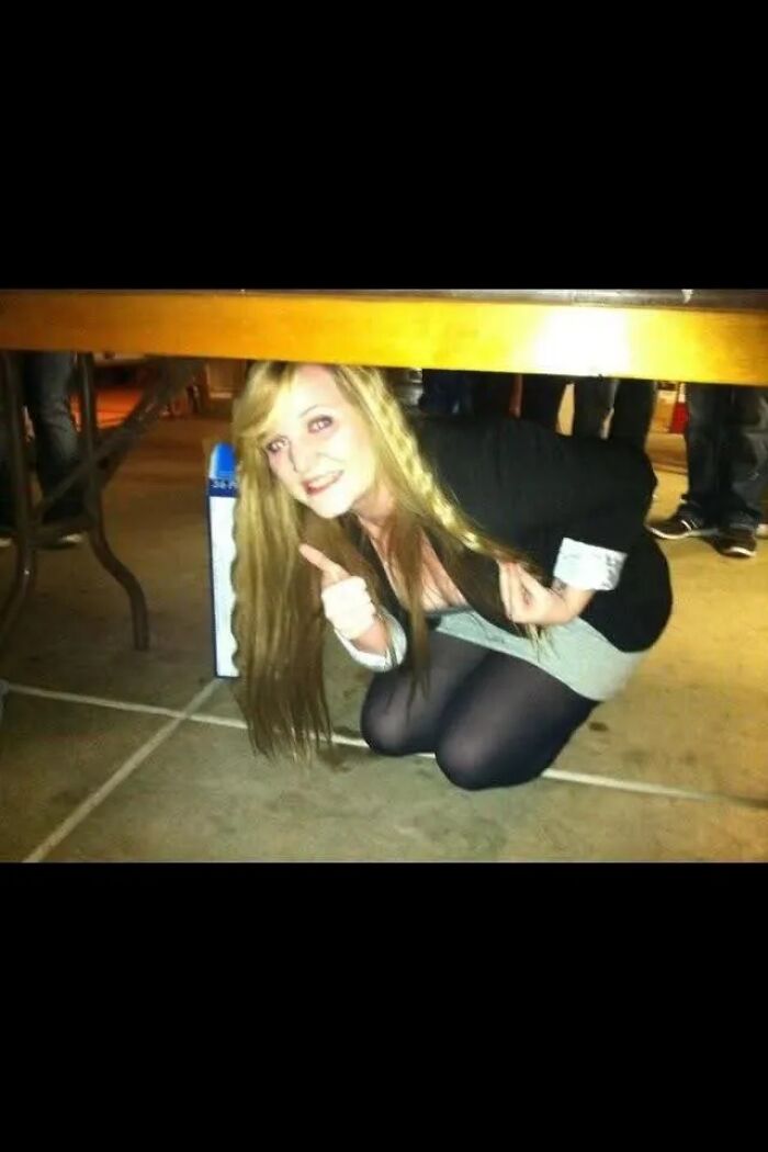Woman crouching under table giving thumbs up