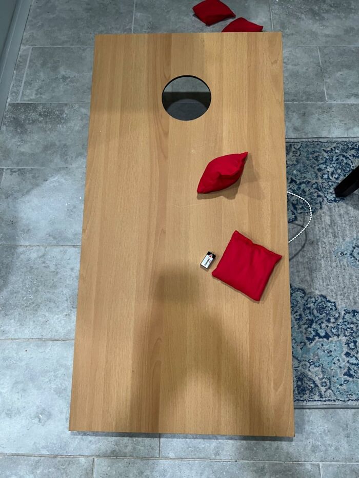 Wooden cornhole board with red bean bags, a popular outdoor backyard essential for summer fun.