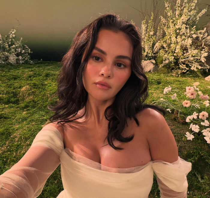 Selena Gomez taking a selfie in a white dress surrounded by flowers, sparking pregnancy rumors among fans.