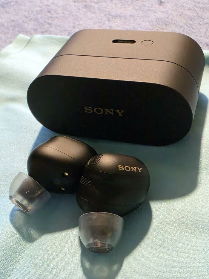 Black Sony earbuds and their charging case on a light blue fabric, part of the Prime Day Deals for electronics.