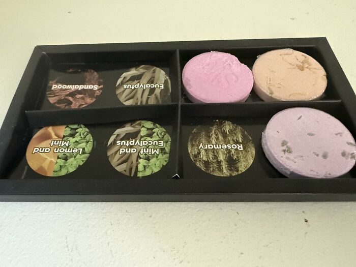 A black tray with three colorful bath bombs and labels for sandalwood, eucalyptus, lemon & mint, and rosemary scents, ready for Prime Day Deals.