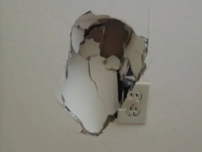 A large hole in a white wall with a power outlet dislodged, representing an unserious ER visit.