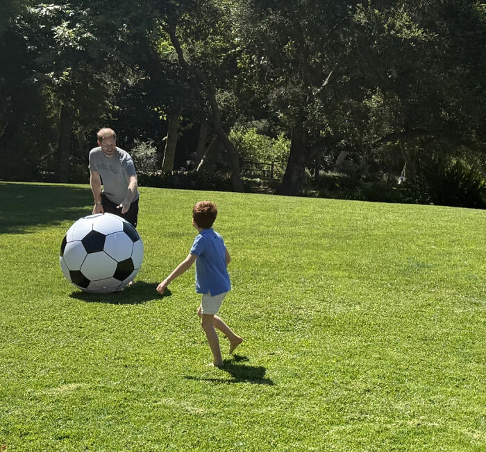 Man and child playing with a giant soccer ball on a green lawn