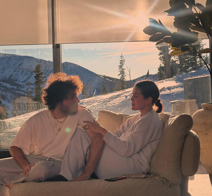 Selena Gomez and a male companion on a couch in a snowy setting, leading to fan speculation about her being pregnant.