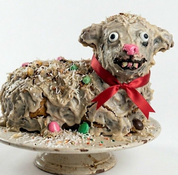 A hilariously messed up cake resembling a lamb with a creepy face and a red ribbon.