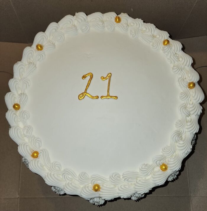 A hilariously messed up cake, a white round cake with gold number 21 and gold sprinkles around the edge.