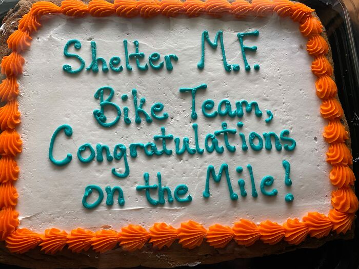 Hilariously messed up cakes: A white cake with orange frosting around the edges that reads Shelter MF Bike Team, Congratulations on the Mile!