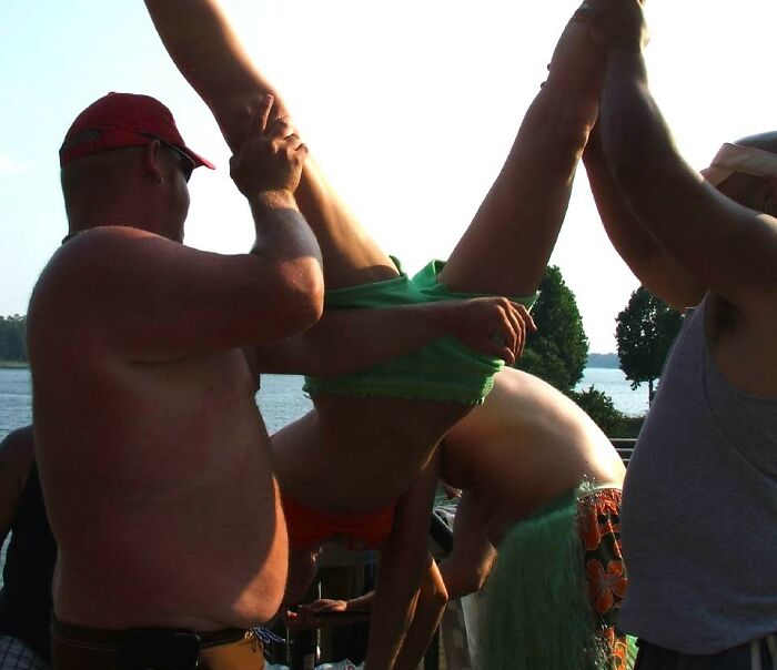 Group of people holding a person upside down near a lake