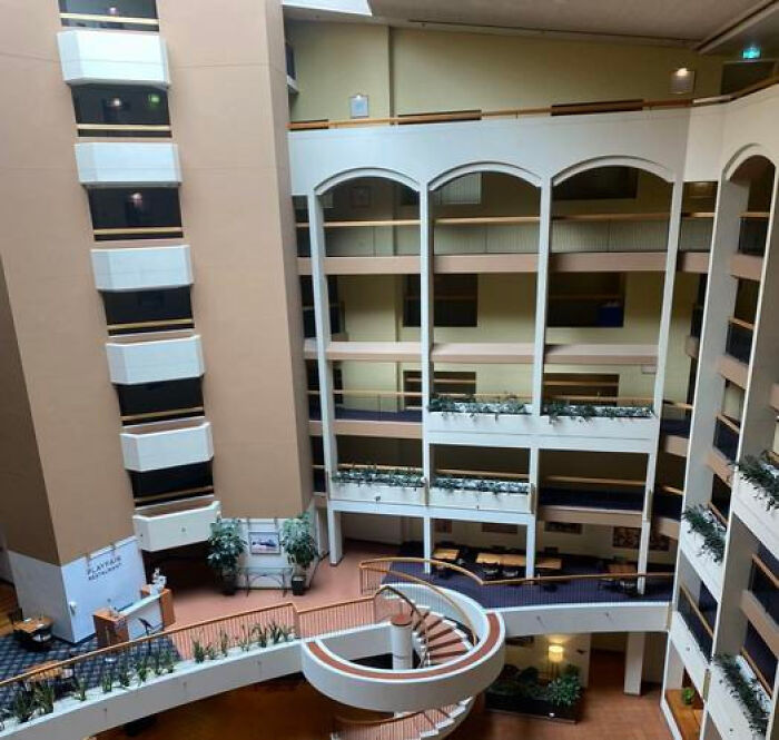 A vast, empty hotel atrium with multiple floors and a spiral staircase, a haunting liminal space.