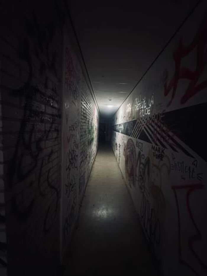 A dark, haunting liminal space, a narrow hallway covered in graffiti, lit by a distant light source.