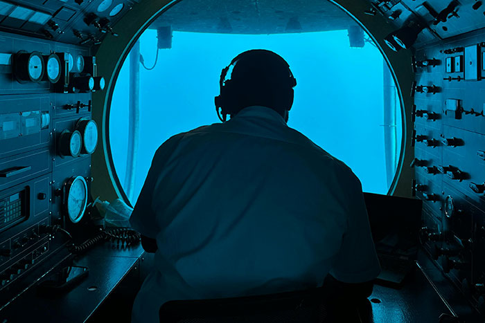 Man inside submarine viewing panel in deep sea with control instruments