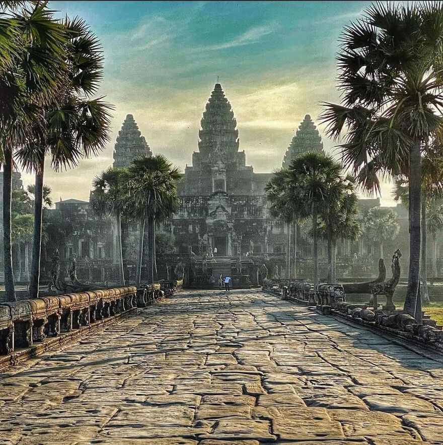 Ancient temple Angkor Wat with stone pathway and palm trees at sunrise