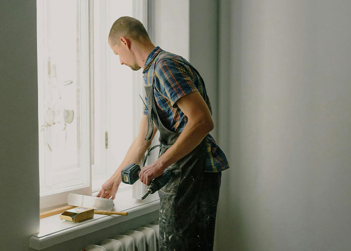 Man in work clothes measuring a window frame during home repair