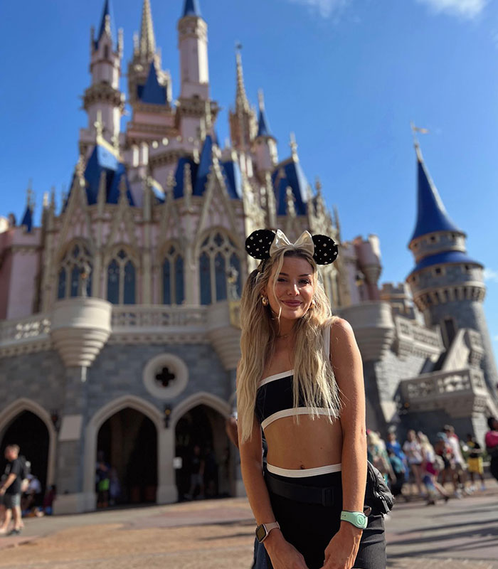 Woman in Mickey ears posing in front of Disney castle at theme park Woman in Mickey ears posing in front of Disney castle at theme park