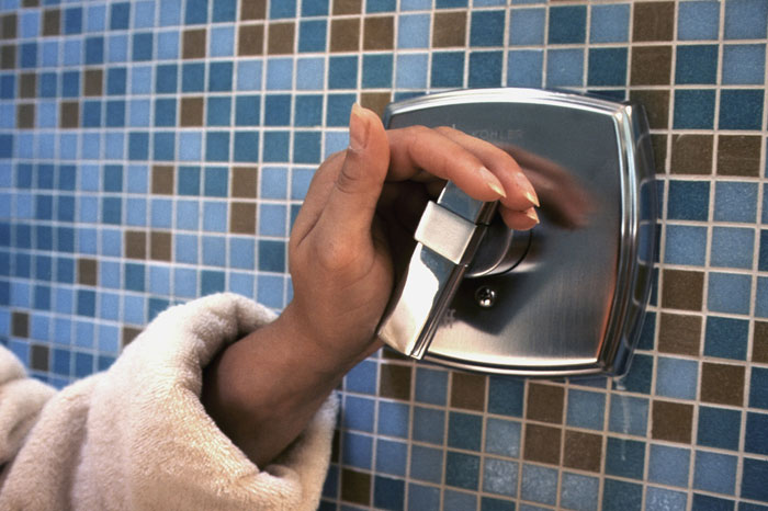 Hand turning shower k**b against blue tile wall