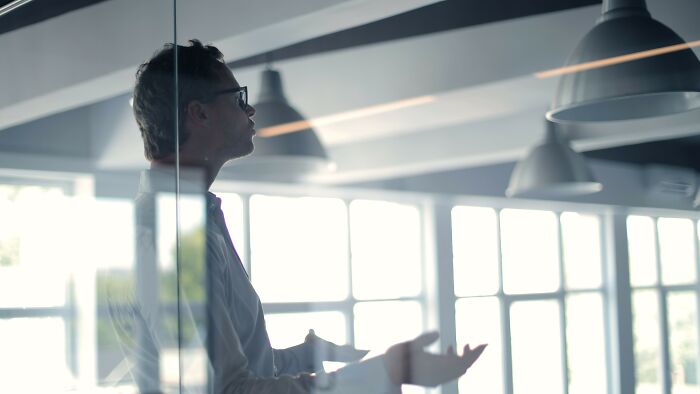 Man in office gesturing thoughtfully in glass room reflecting moral dilemma decision