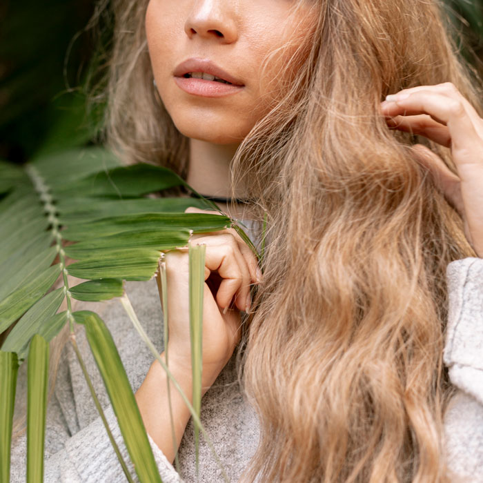 Partial view of woman with long hair and green leaves emphasizing natural beauty