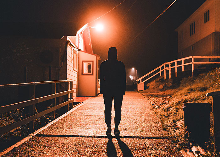 Person standing on dimly lit street at night realizing time to leave immediately