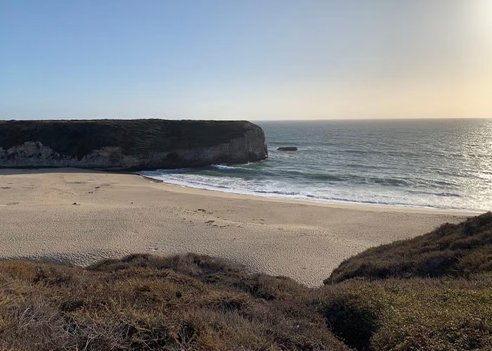 Empty sandy California beach with ocean waves and rocky cliff in background Empty sandy California beach with ocean waves and rocky cliff in background