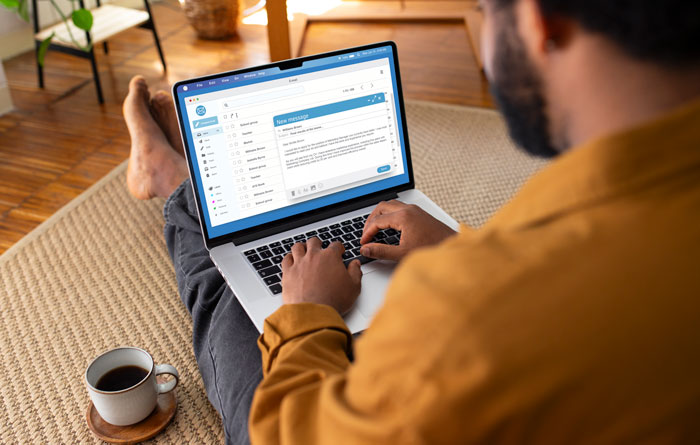 A man sitting on the floor with a coffee, using a laptop, perhaps discovering DNA testing stories online.