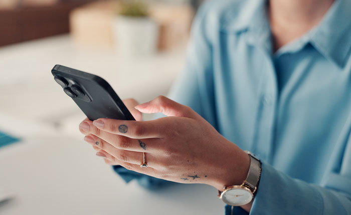 A person's hands holding and typing on a smartphone with a watch on their wrist. This image relates to things people saw on their late parents' phones.