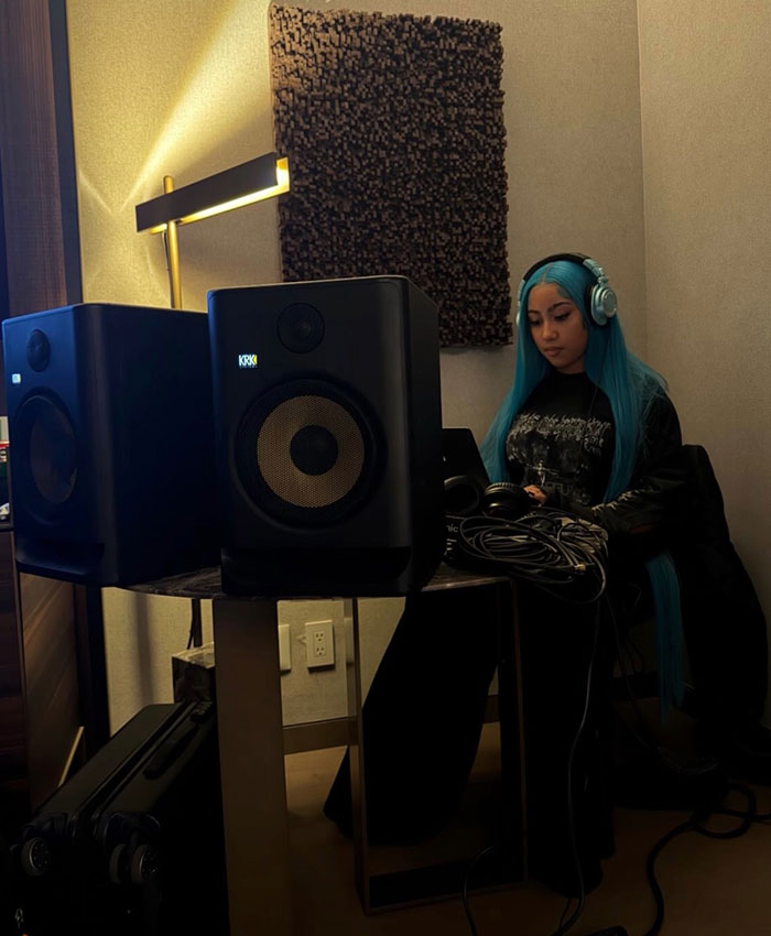A woman with blue hair at a sound mixing desk, wearing headphones.