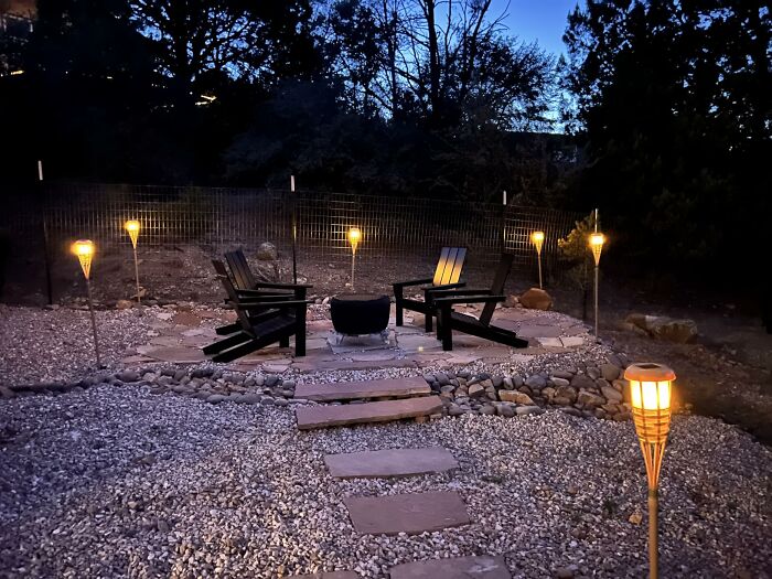 A cozy outdoor backyard patio at dusk with illuminated tiki torches, Adirondack chairs, and a fire pit, perfect for summer essentials.
