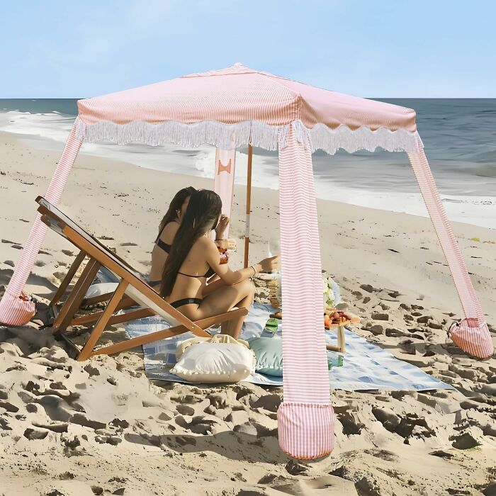 Two women relaxing under a pink striped beach tent, enjoying outdoor summer ease with Prime Day backyard essentials.