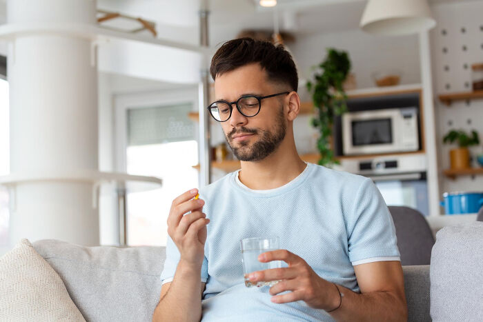 Man carefully taking a pill with water, contemplating unhinged breakup excuses