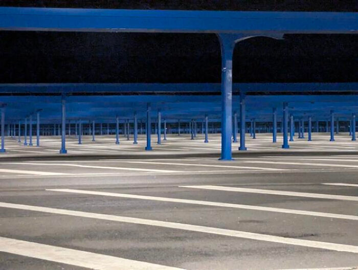 An empty, blue-columned parking garage at night, creating a haunting liminal space.
