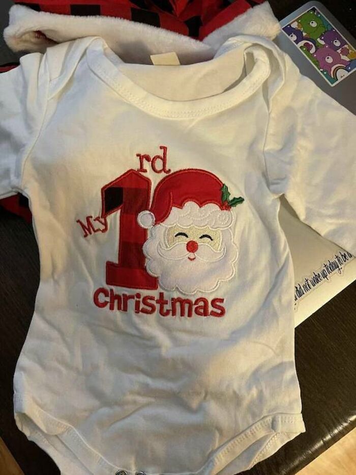 A white baby onesie with a red Santa Claus image and text that mistakenly reads “My 1rd Christmas”, a “You Had One Job” Fail.