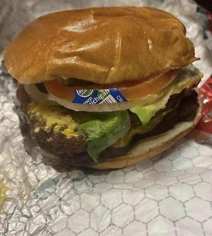 A hamburger with a Michigan produce sticker still on its onion, a you had one job fail.
